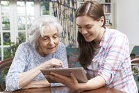 Jugendliche erklärt Seniorin die Funktionsweise eines Tablets
