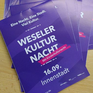 Mehrere Flyer der Weseler Kulturnacht liegen ausgebreitet auf einer Theke 