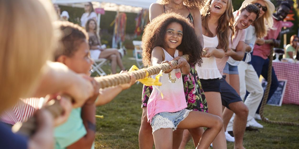 Erwachsene und Kinder beim Tauziehen auf einem Gartenfest bei Sonnenschein