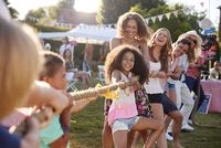 Erwachsene und Kinder beim Tauziehen auf einem Gartenfest bei Sonnenschein