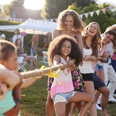 Erwachsene und Kinder beim Tauziehen auf einem Gartenfest bei Sonnenschein